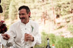A person in a white medieval shirt smiles while holding a drink at an outdoor celebration.