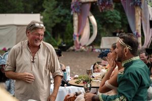 Two people having an animated conversation at an outdoor gathering with decorative tents and draping in the background.