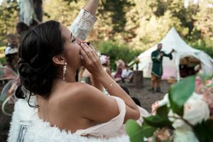 Someone celebrates joyfully in a white dress at an outdoor wedding reception with tents visible.
