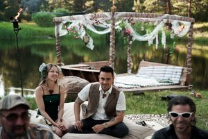 A decorated outdoor lounge area near a pond with white fabric and floral arrangements overhead.