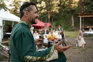 Someone in green attire gestures enthusiastically during an outdoor celebration among scattered tents and tables.