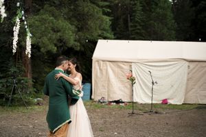 Wedding couple embraces intimately near canvas tent in forest setting.