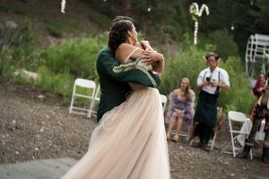 A couple shares their first dance at an outdoor wedding reception surrounded by guests and pine trees.