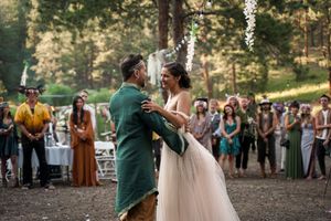 Outdoor wedding reception with guests gathered among pine trees at sunset.