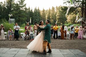 Outdoor forest wedding reception with couple dancing surrounded by guests.