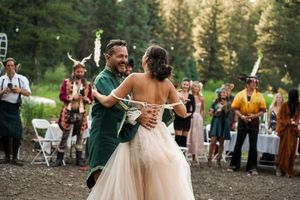 Wedding celebration on an outdoor dance floor surrounded by pine trees at sunset.