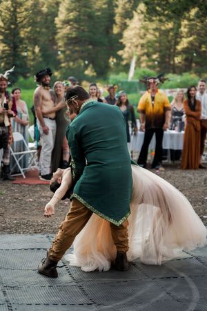 A dramatic dance dip during a wedding reception on an outdoor dance floor with guests watching in the background.