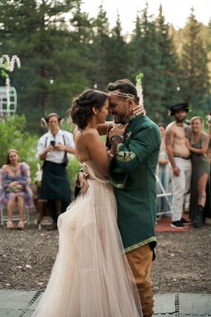 Intimate dance moment at outdoor wedding with forest backdrop and watching guests.
