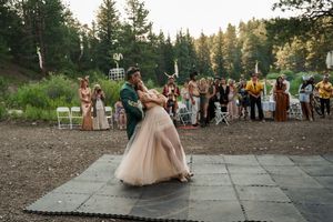 Wedding guests dance and celebrate on an outdoor patio surrounded by forest scenery.