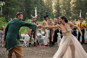 Dancing couple spins joyfully at an outdoor woodland wedding reception.