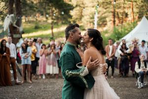 A couple shares an intimate first dance at their outdoor forest wedding surrounded by guests in colorful attire.