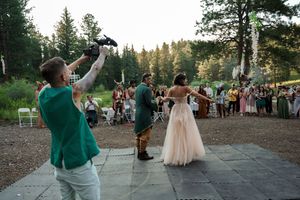 Guests dancing outdoors at a wedding celebration with trees in the background during golden hour.
