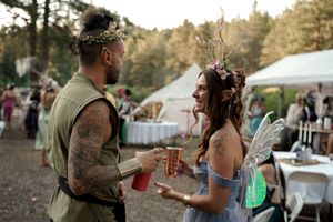 Two festival attendees in medieval-inspired outfits enjoy drinks at an outdoor celebration.