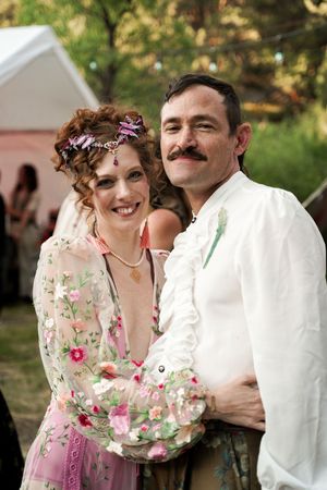 A couple shares a romantic dance moment outdoors wearing floral and white attire at a casual outdoor wedding event.