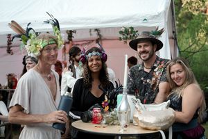 An outdoor gathering with people wearing floral headdresses and medieval costumes sharing drinks.