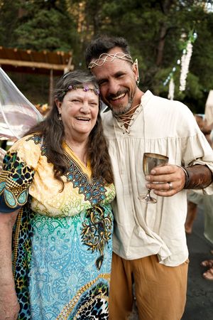 A couple laughs and dances together at an outdoor event, with the woman wearing a turquoise dress with gold accents.