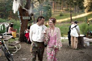 Guests enjoy an outdoor wedding celebration in a rustic woodland setting with pink floral decorations.