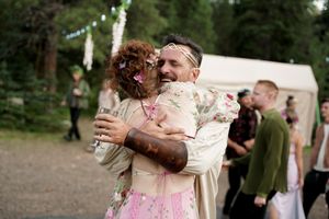 A couple embraces while dancing at an outdoor celebration, both covered in pink powder.