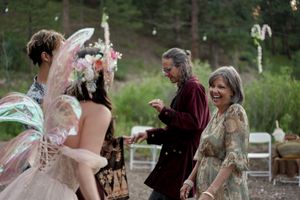 Wedding guests laugh and share joyful moments during an outdoor reception in a wooded setting.