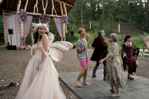 People dancing and celebrating at an outdoor wedding with fairy wings and casual attire.