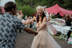 A joyful outdoor wedding celebration with people dancing under strings of decorative lights.