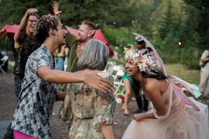 Joyful partygoers dance and laugh together at a festive outdoor celebration in the woods.