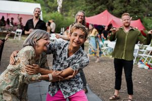 Guests share laughter and dance at a casual outdoor party with red tents in the background.