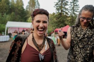 A guest shares an enthusiastic laugh at an outdoor event with trees and white tents in the background.