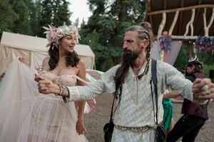 Two people in whimsical medieval costumes dance together at an outdoor renaissance festival.