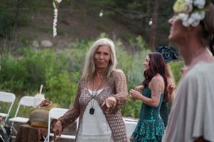 Festival attendees in flowing dresses dance and celebrate at an outdoor gathering with trees in the background.
