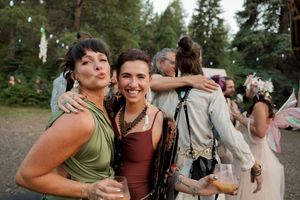 Festive guests enjoy drinks and laughter at an outdoor woodland celebration with string lights overhead.