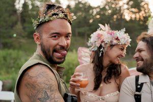 Wedding guests wearing floral crowns celebrate with drinks at an outdoor forest reception.
