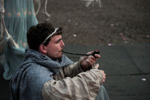 Costumed actor in gray winter clothing points prop pistol during theatrical performance.