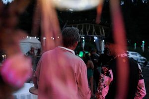 Back view of someone in pink at an outdoor evening event with stage lights.