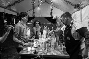 Party guests gather under a tent decorated with hanging greenery and string lights.