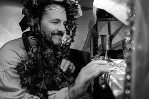 A monochrome image of someone wearing a floral crown examining an object in medieval attire.