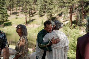 Wedding guests share emotional embraces during an outdoor forest ceremony.