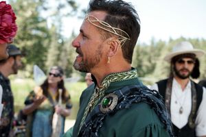 Wedding attendee wearing an ornate headpiece and emerald green ceremonial attire in a forest setting.