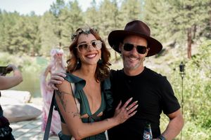 A festive outdoor gathering with people wearing sunglasses and hats in a wooded setting.