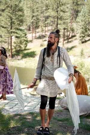 Guest in medieval-inspired white attire holds parasols at a woodland wedding.