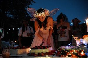 Whimsical fairy figure illuminated at night among decorative table settings and candles.