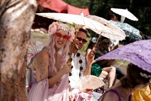 Wedding guests holding decorative parasols share laughter under sunny skies.