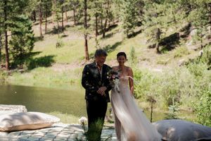 A wedding couple posing by a serene lake with pine-covered hills in the background.