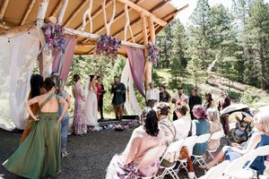 An outdoor wedding ceremony setup with purple floral decorations and a wooden pergola.
