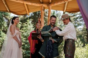 An intimate moment unfolds during an outdoor wedding ceremony beneath a rustic wooden pavilion with floral decor.
