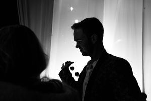 A silhouetted figure gestures while speaking in front of a bright backlit curtain or screen.