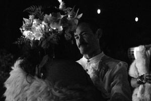 A black and white scene of two people in medieval costumes at a nighttime festival.