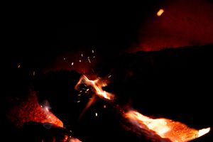 A glowing campfire illuminates the darkness with sparks and flames.