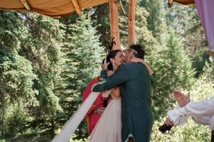 Couple shares their first kiss under a draped canopy during forest wedding ceremony.