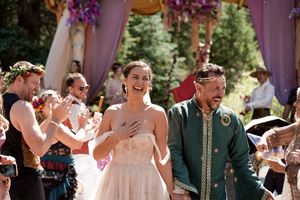 Guests celebrate during a wedding ceremony under a flower-adorned wooden structure in a garden setting.